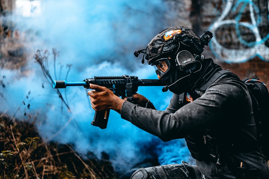 A soldier in full tactical gear aims with precision through blue smoke, ready for action.