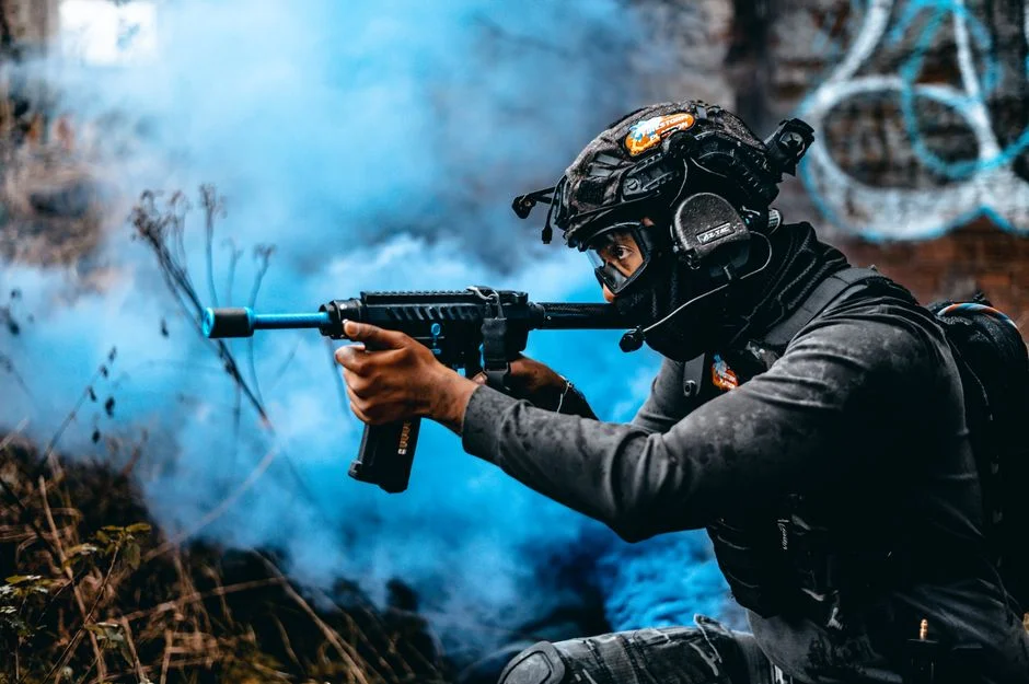 A soldier in full tactical gear aims with precision through blue smoke, ready for action.